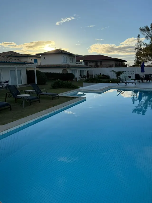 Piscina azul com espreguiçadeiras e as casas da pousada ao fundo