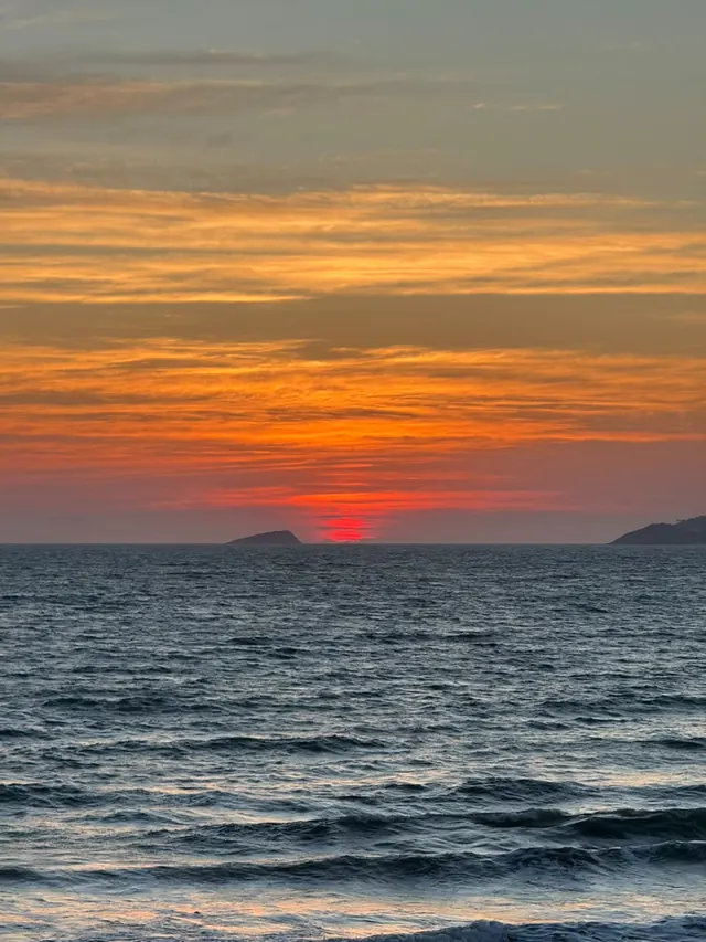 Sol vermelho nascendo no mar entre duas ilhas