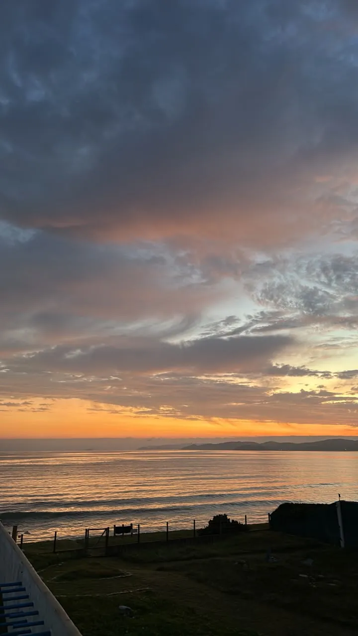 Pôr do sol entre nuvens sobre o mar, visto do jardim